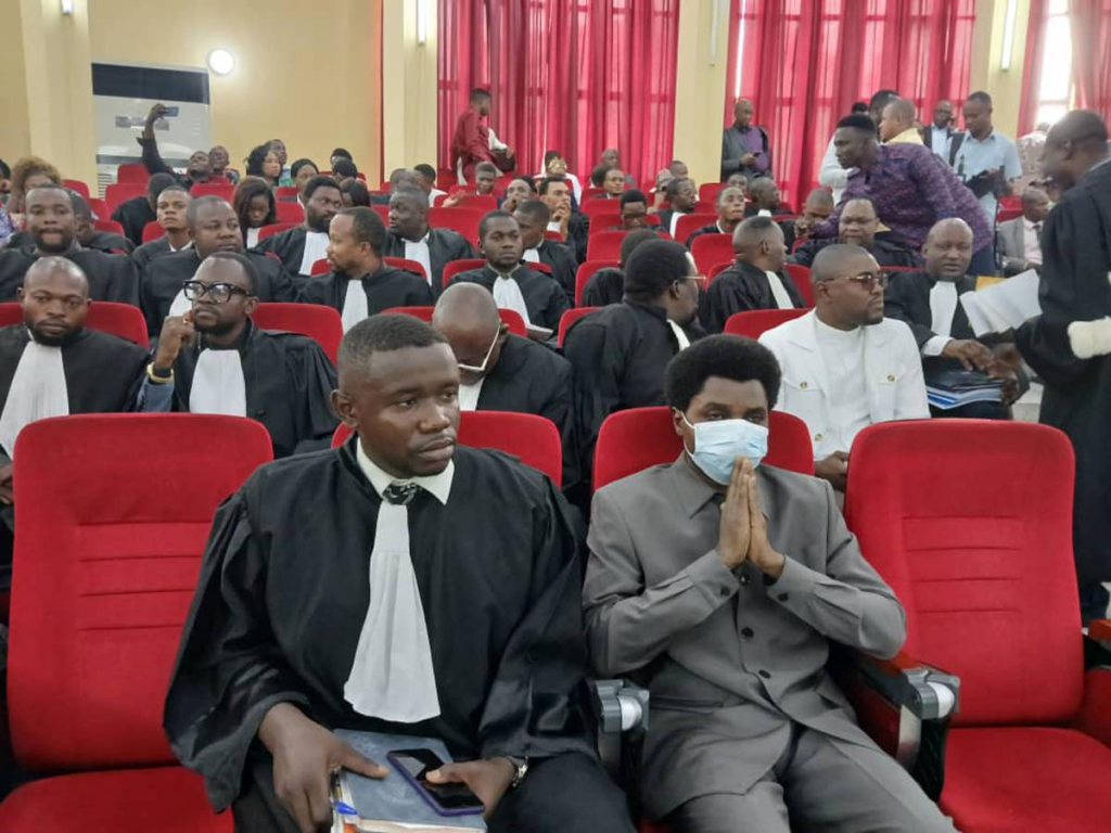 Constant Mutamba (au centre, en costume) entouré de ses avocats lors de l’audience du 23 juillet 2025 devant la Cour de cassation à Kinshasa. Ce jour-là, le tribunal a rejeté les exceptions de procédure soulevées par la défense et a entamé l’examen des faits reprochés au prévenu