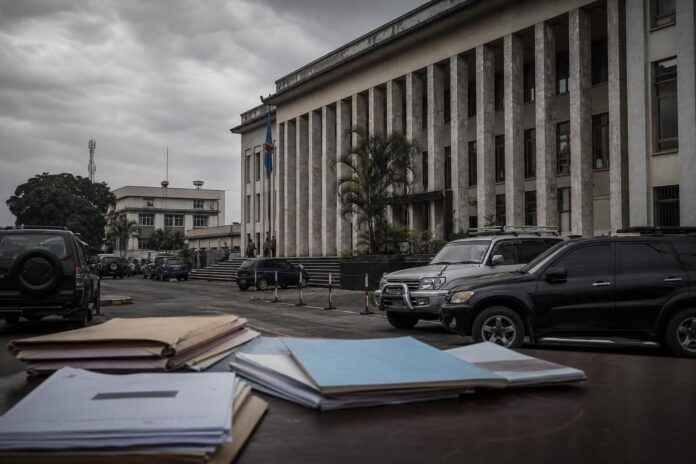 Bâtiment institutionnel à Kinshasa avec documents politiques et ambiance de tension autour de la reprise des activités du PPRD