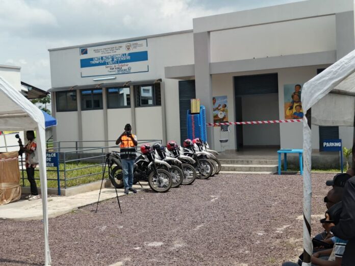 batiment de centre de sante en zone periurbaine de Nsele avec ambulance stationnee et patients attendant a l'entree
