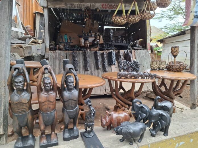 Des sculptures et objets d'art exposés au marché Gondola à Matadi, avec des clients potentiels passant à côté