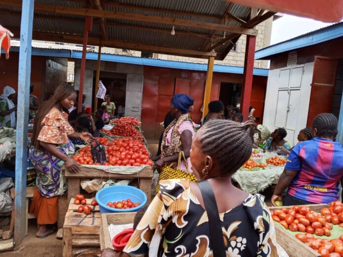 Marché bondé à Beni avec étals de produits vivriers et affichage de prix