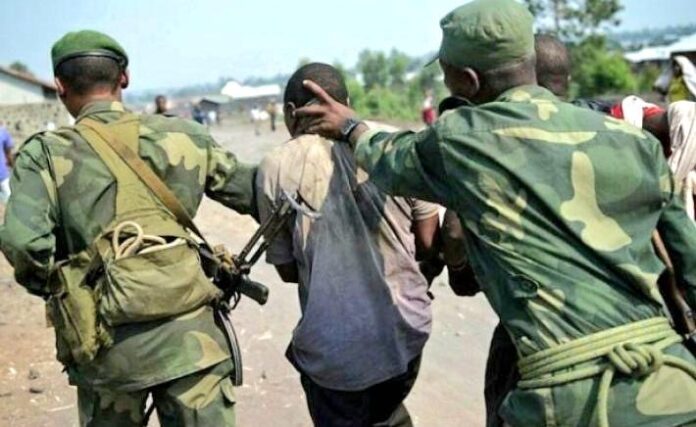 Rue sombre de Bulongo après une fusillade, avec présence discrète des forces de sécurité et habitants à distance
