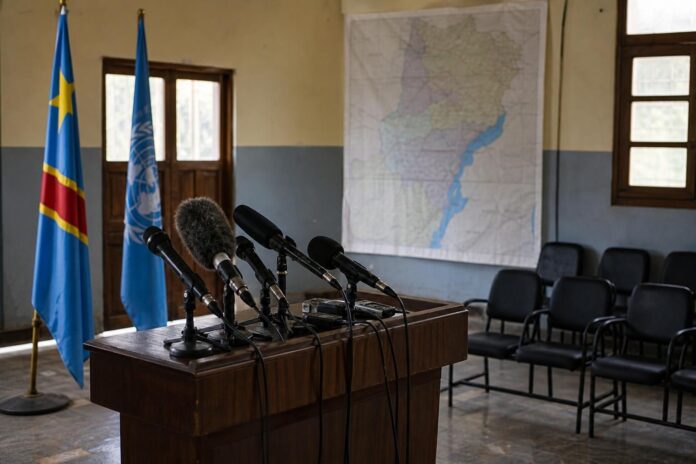 Salle de presse officielle a Bunia avec pupitre, micros et drapeaux dans un contexte de crise securitaire en Ituri