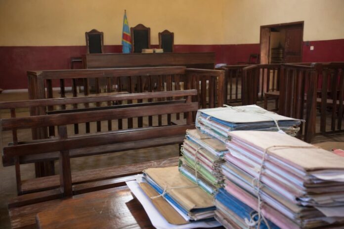Salle d'audience sobre avec bancs, dossiers judiciaires et magistrats lors d'une session foraine a Kalemie