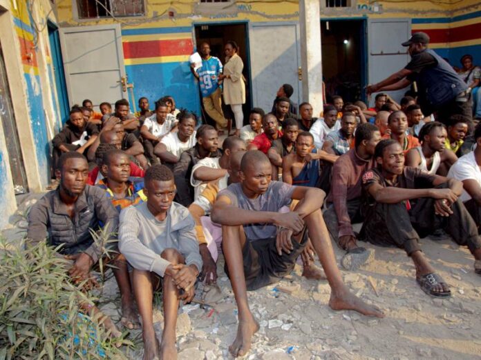 forces de police deployees dans une rue dense de Kinshasa pres de constructions precaires en cours de demolition