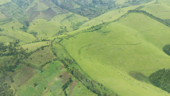 Collines de Masisi sous tension avec fumée au loin, route de terre et villages exposés aux affrontements près de Ngungu et Rubaya