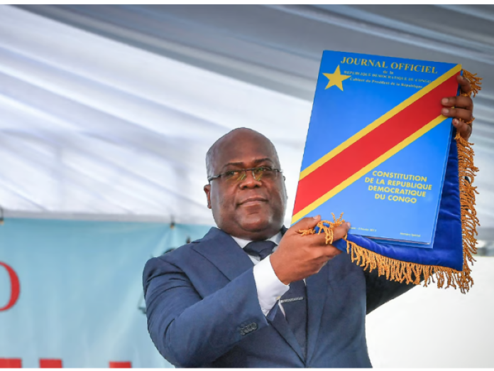 Microphone de direct audio devant un décor institutionnel évoquant un débat politique sur la révision constitutionnelle en DRC