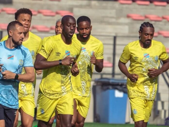 Terrain d'entraînement avec ballons, plots et but, drapeau congolais en fond, symbolisant la préparation de l'équipe nationale pour le