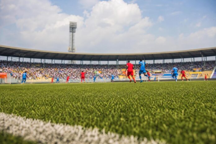 Joueurs de football s'affrontant sur un terrain, maillots rouges et bleus, stade rempli