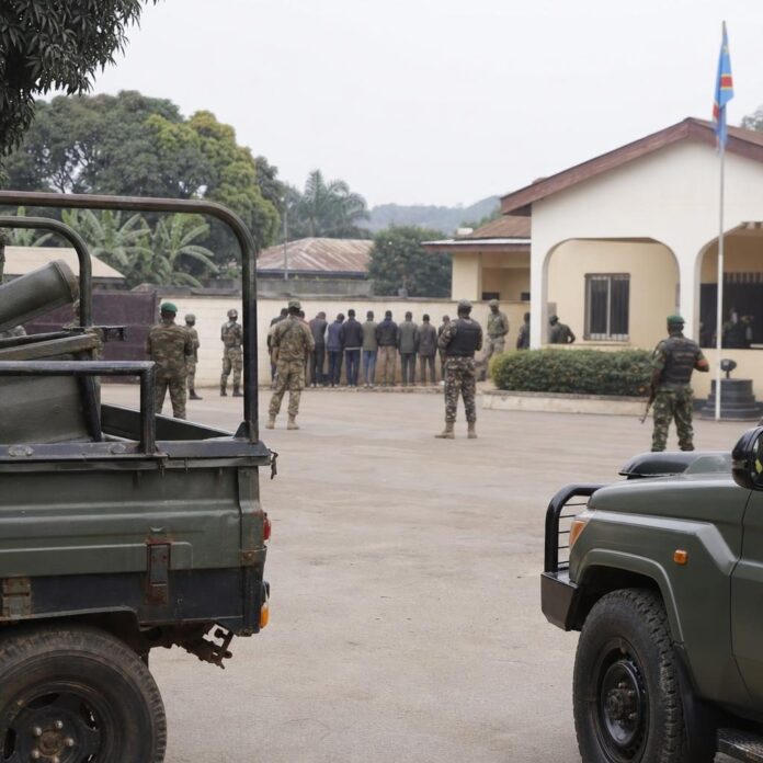Militaires en position de sécurité lors de la présentation de présumés soutiens des ADF dans une cour administrative à Isiro