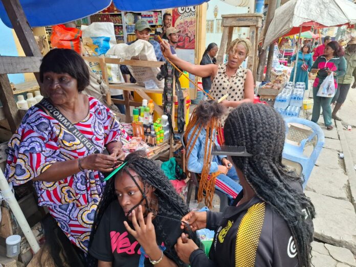 Femmes et jeunes filles se faisant tresser les rastas dans un salon de coiffure à Matadi