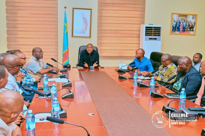 Salle de réunion avec des participants assis, une table au premier plan, une bannière de sensibilisation contre Ebola