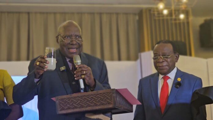Deux professeurs debout derrière un pupitre avec des livres exposés lors d'une cérémonie de lancement à Kinshasa