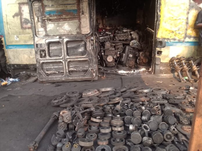Étal de pièces détachées automobiles, moteurs et pneus exposés à même le sol au marché Wenze ya Mitraille à N'djili, Kinshasa
