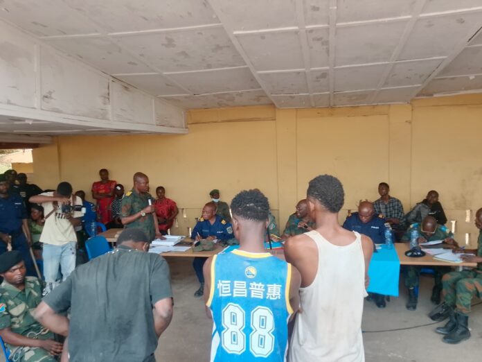 Audience foraine du tribunal de garnison à Bandundu, avec des juges à une table et un public attentif dans un cadre public