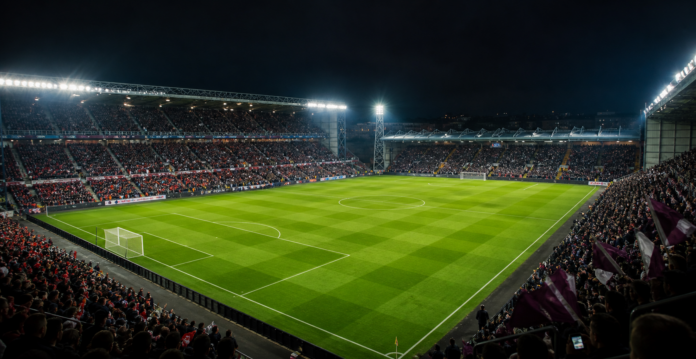 Vue large d un stade ecossais sous les projecteurs avec une equipe bordeaux face a une equipe grenat.