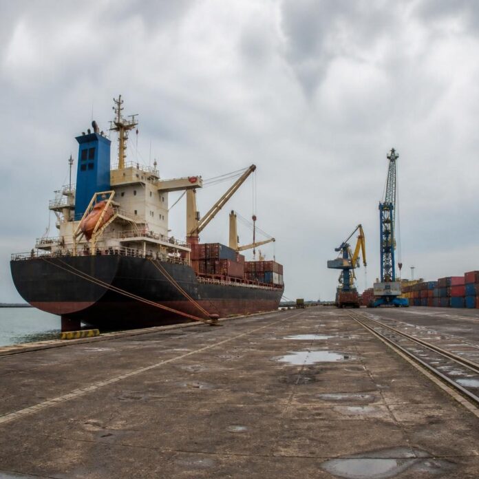 Navire de marchandises à quai au port de Boma, conteneurs et grues visibles, ambiance calme