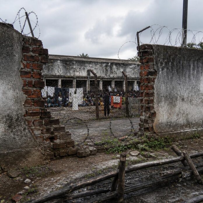 Cour surpeuplée de la prison centrale de Boma avec murs dégradés et clôture partiellement effondrée