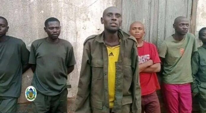 Des hommes en tenue militaire déposant des armes devant des soldats dans un paysage de collines arides au Sud-Kivu