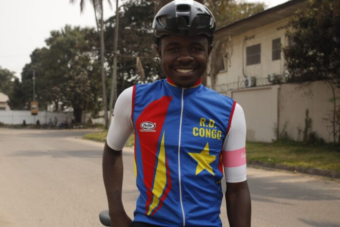 Cycliste sur vélo de gravel sur une piste en terre, vu de dos, avec casque, sous le soleil africain