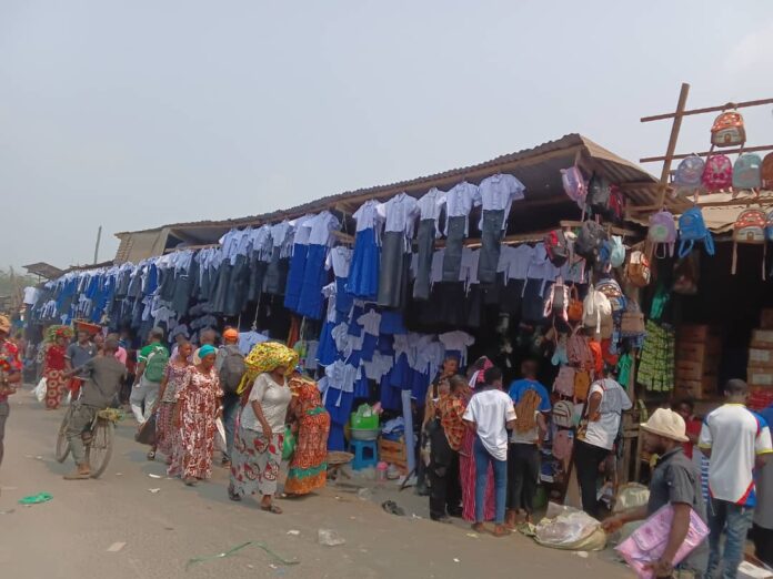 Cahiers, sacs et uniformes scolaires exposés sur un étal au marché central de Kindu, avec peu de clients