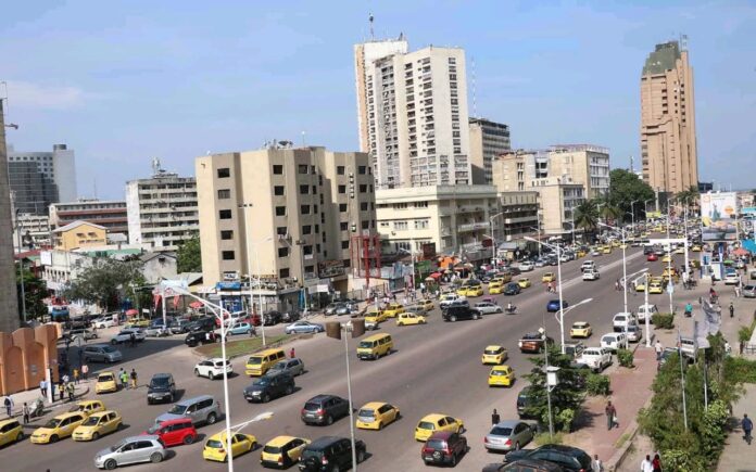 Un quartier de Kinshasa avec des annonces de location et des maisons modestes, illustrant la pression sur le marché locatif