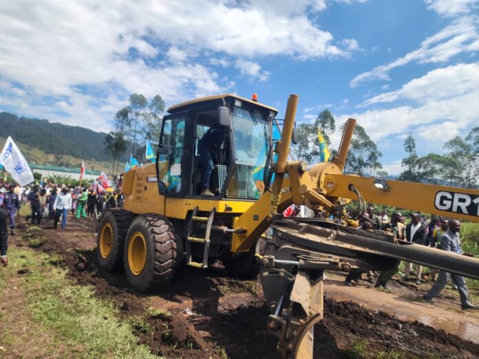Piste en terre battue en cours de nivellement, entourée de collines et d’engins de chantier