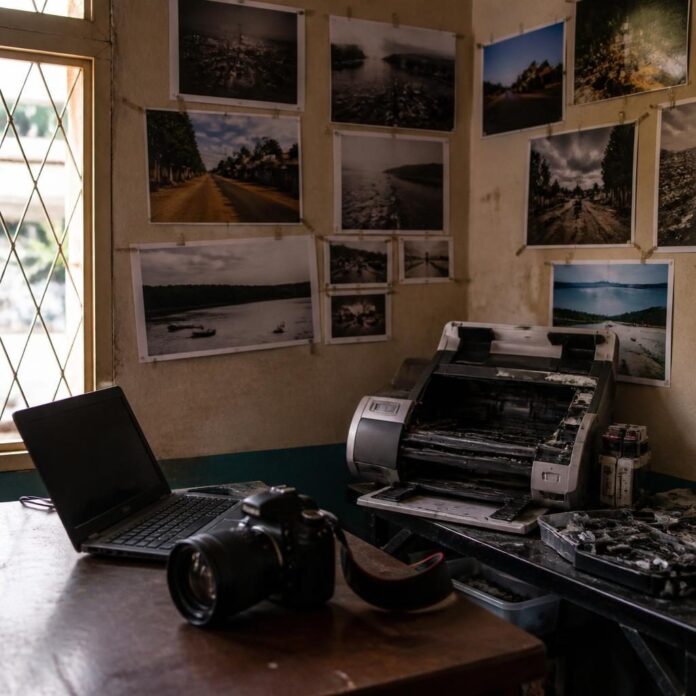 Un studio photo à Kindu avec des tirages exposés, un ordinateur et une imprimante en panne, sans personne reconnaissable