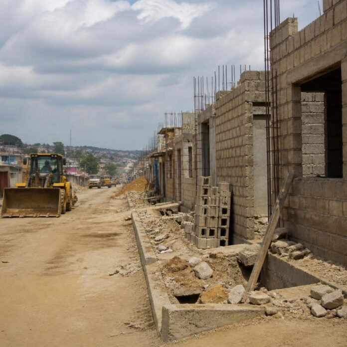 Maisons construites sur une emprise routière à Matadi, avec des engins de chantier en arrière-plan