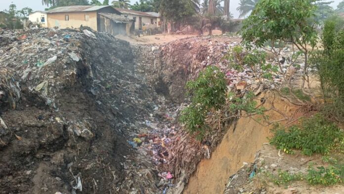Ravin d'érosion menaçant des habitations à Muanda, avec des caniveaux obstrués par du sable et des herbes sauvages