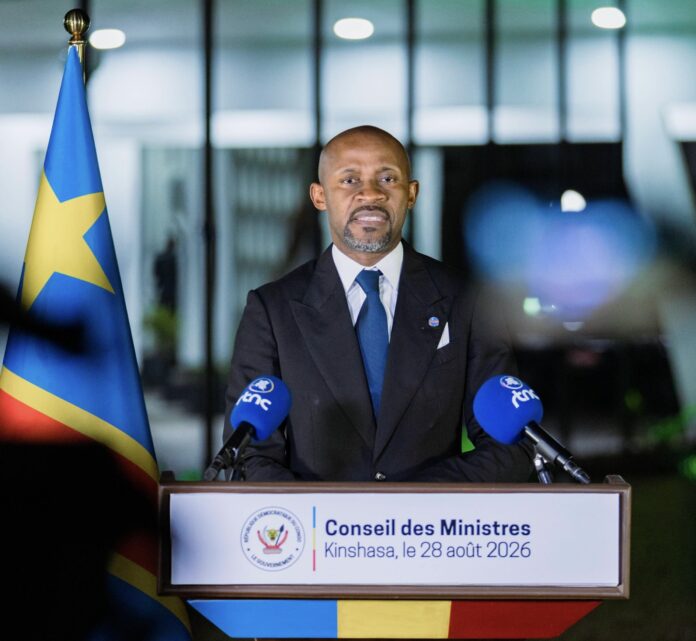 Salle de réunion gouvernementale avec écran affichant des symboles de réseaux sociaux et drapeau congolais