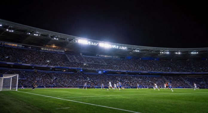 Vue large d un match nocturne entre une equipe en blanc et une equipe bleu et blanc.