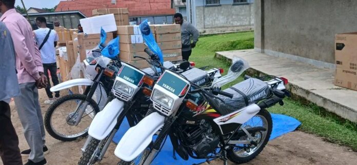 Ambulance blanche et motos devant un bâtiment administratif à Tshopo lors de la remise de matériel médical