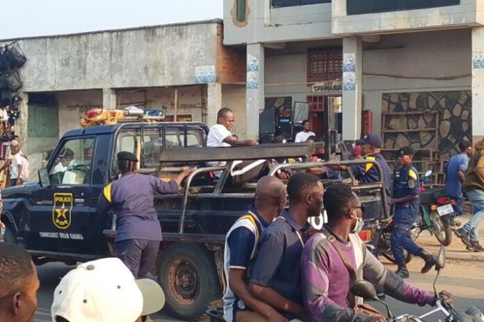 Des policiers en tenue anti-émeute alignés dans une avenue de Lubumbashi, avec des barricades et un nuage de gaz lacrymogène