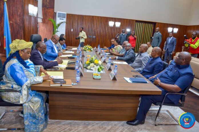 Salle de réunion institutionnelle à Kinshasa avec table, micros et dossiers parlementaires