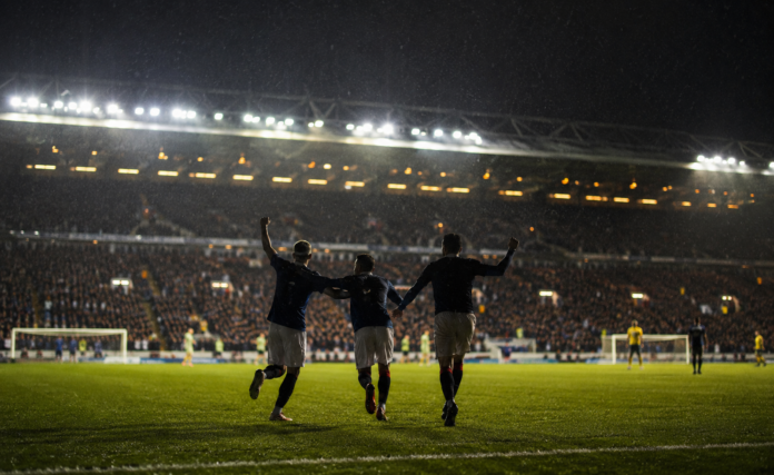Joueurs anonymes célébrant une victoire sous la pluie dans un stade britannique