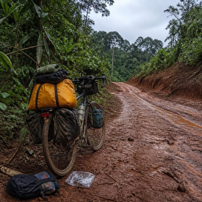 Vélo de voyage chargé de sacoches sur une route de terre bordée de forêt tropicale près de Ouesso