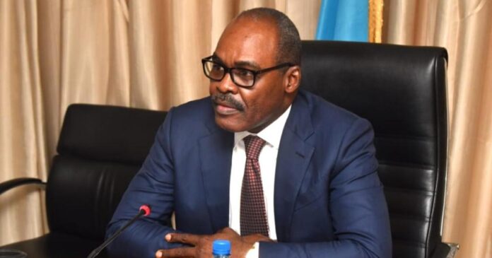 Micros et pupitre dans une salle de presse à Kinshasa, documents et notes sur la table, ambiance de déclaration politique