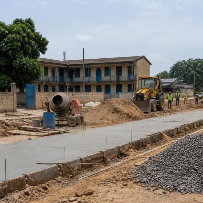 Engins de chantier et ouvriers sur une route en terre devant un bâtiment scolaire à N'Djili, Kinshasa
