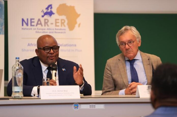 Salle de conférence universitaire à Bruxelles avec pupitre, micros et documents, évoquant un débat Afrique-Europe