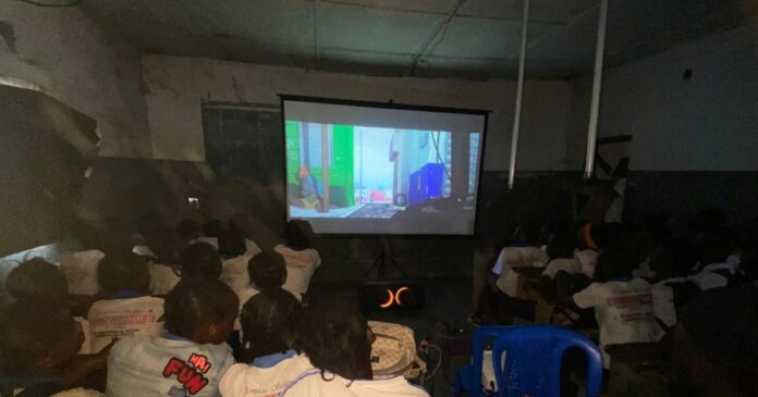 Des élèves dans une salle de classe transformée en salle de projection, regardant un film sur un écran blanc