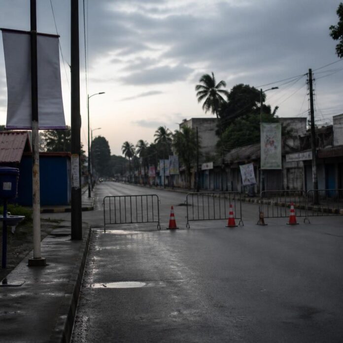 Rue de Kisangani barriérée par des policiers à l'aube, avec affiches de sensibilisation sanitaire sur la riposte Ebola