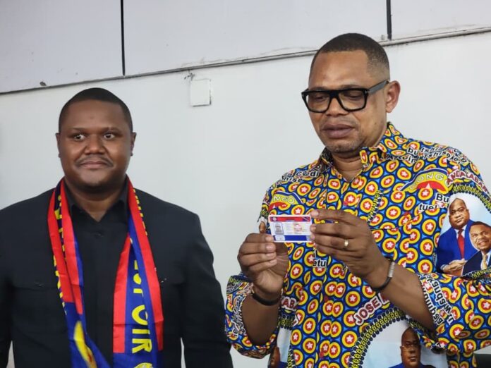 Estrade et salle décorées pour une cérémonie politique à Kinshasa, avec piles de cartes de membres et rubans roses