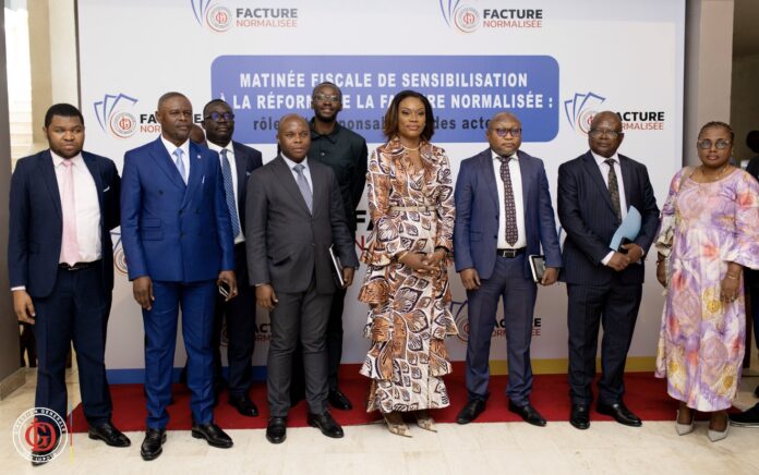 Salle de conférence à Kinshasa avec tables en U, documents fiscaux, ordinateurs et écran de projection lors d’un atelier sur la facture