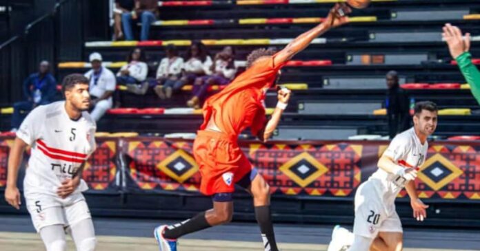 Ballon de handball posé sur le parquet d'une salle africaine avant une demi-finale de clubs, avec les tribunes en arrière-plan