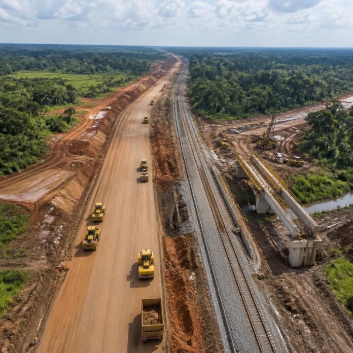 chantier de construction avec plusieurs engins lourds, voie ferrée et terrain bordé de végétation dense