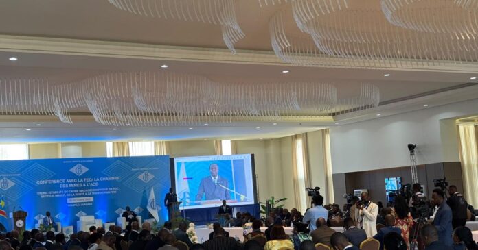 Grande salle de conférence avec un orateur, un grand écran et un public assis, décor bleu à l'avant