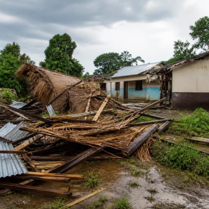 Débris de maisons en matériaux précaires après de fortes pluies, avec toitures arrachées et sol boueux dans un village du Maï-Ndombe