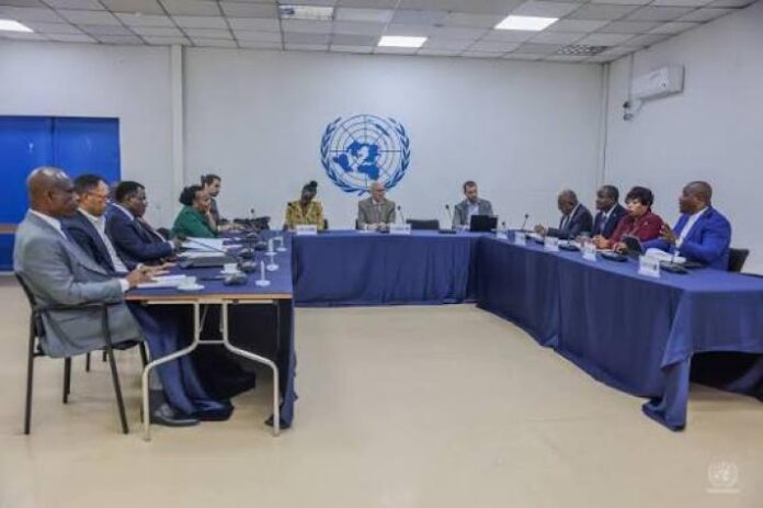 Salle de réunion institutionnelle avec table, micros et documents évoquant des consultations diplomatiques