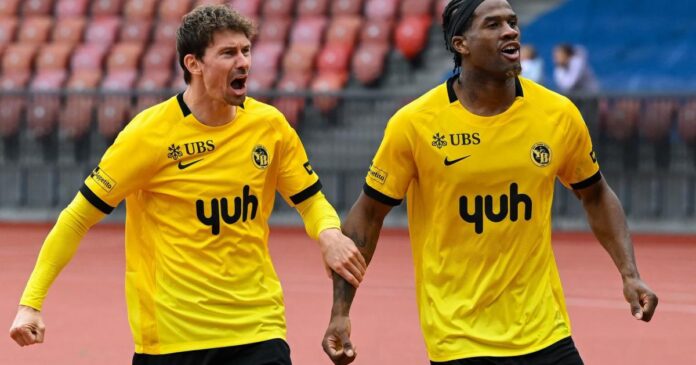 Attaquant en action sur une pelouse suisse, maillot jaune et noir, ballon au pied, stade en arrière-plan